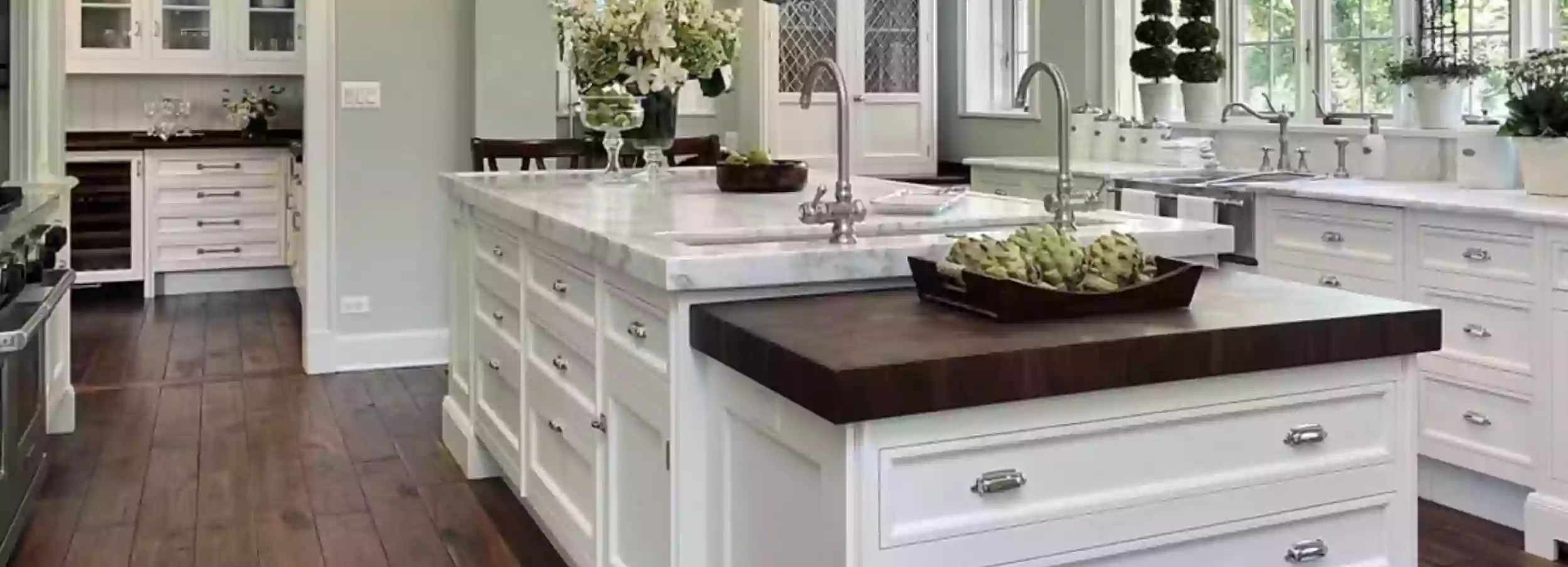 Kitchen island in large, bright modern kitchen with white cabinets and brown floor.