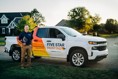 A friendly Five Star Painting estimator holding a project folder in front of his branded truck