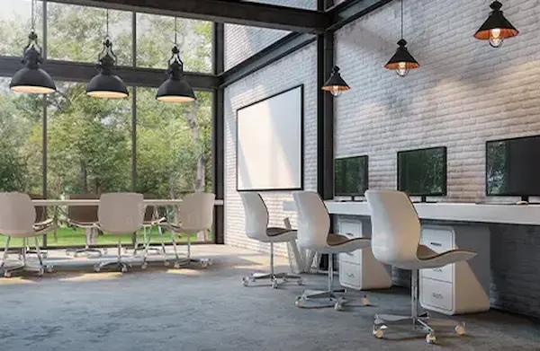 Commercial office space with large windows, a white boards and computer stations along a white wall.