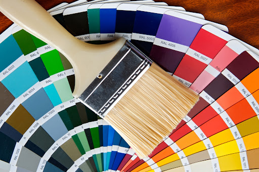 Wooden paint brush surrounded by assorted colored paint swatches.