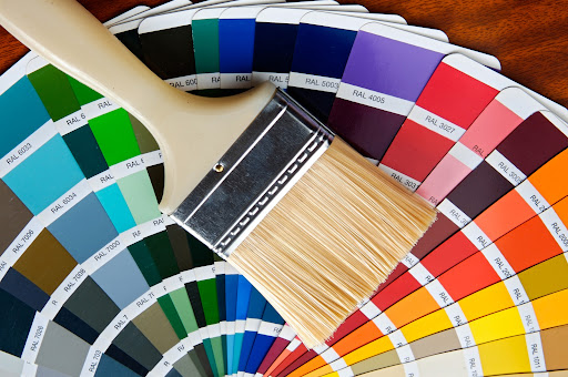 Paint brush resting atop stack of color swatches laid out on table.