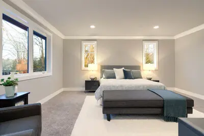 A maser bedrom painted in light gray tones with furniture and bright windows.