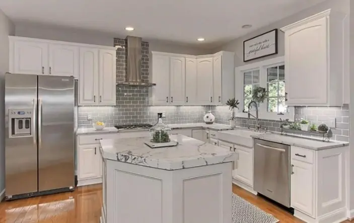 A kitchen with white cabinets, stainless steel fridge and center island.